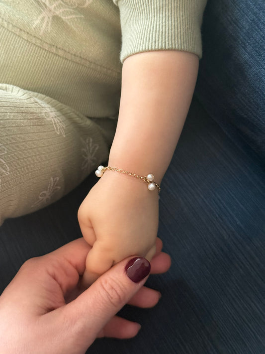 Hand holding a child's hand wearing a pearl bracelet on a dark surface.
