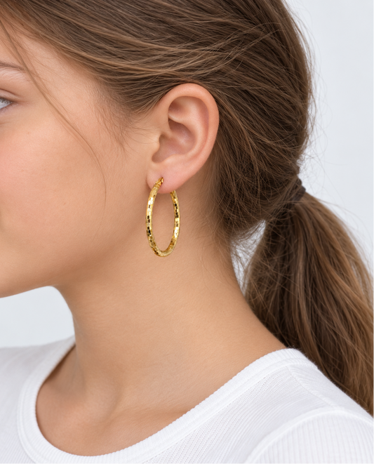A close-up side profile of a young woman wearing a textured gold hoop earring, showing the earring in use on her ear against a clean white background.
