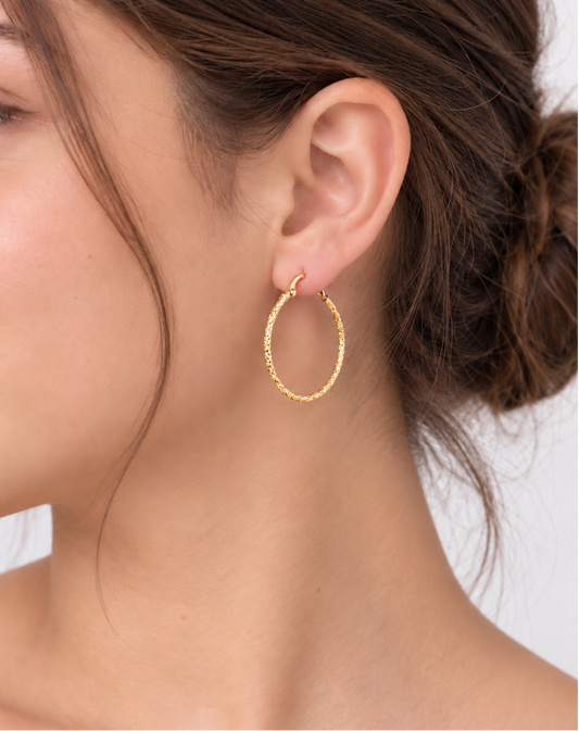 A close-up side profile of a woman wearing a textured gold hoop earring on her earlobe.