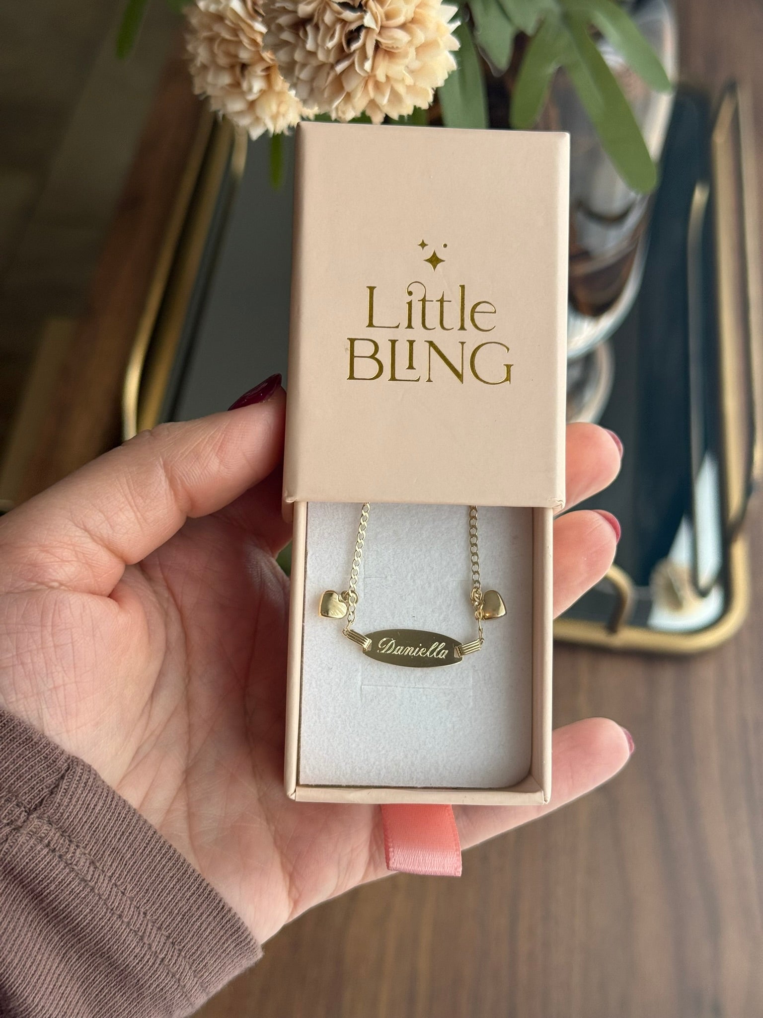 Gold bracelet with 'Danielle' engraving in a 'Little BLING' box held by a hand.