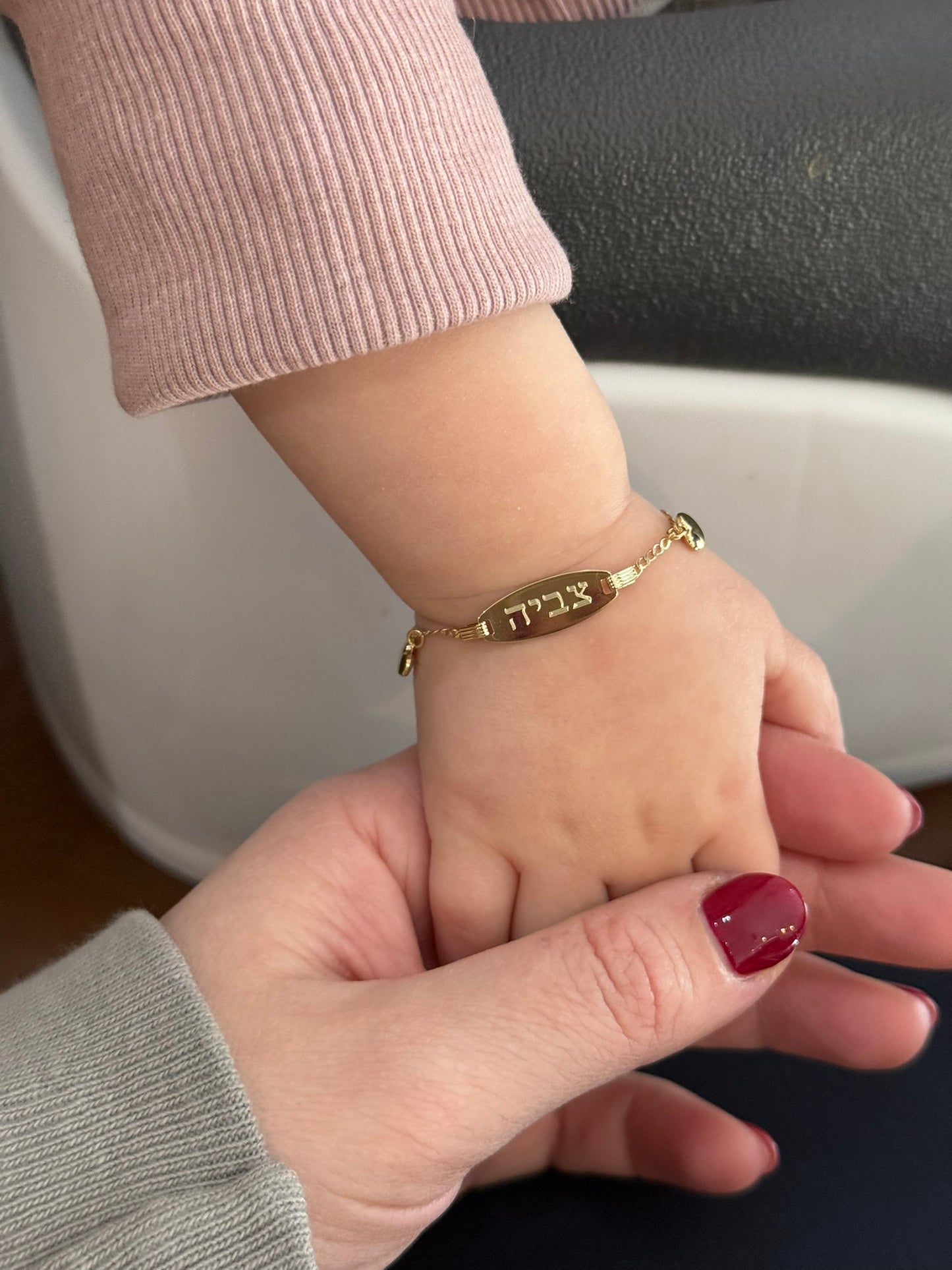 Two hands holding each other, one wearing a gold bracelet with Hebrew text.