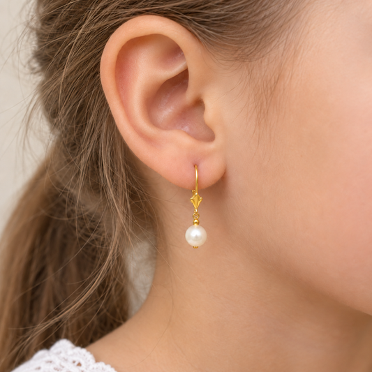A close-up of a person's ear wearing a delicate gold dangle earring with a single white pearl drop, against a soft neutral background.