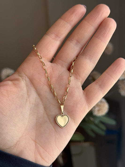 Gold heart-shaped pendant bracelet on a hand with a blurred background
