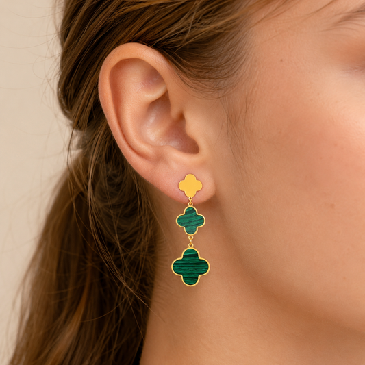 A close-up of a model's ear wearing a double drop earring. The earring features two interlocking four-lobed clover shapes, one in yellow enamel and the other in green enamel, both outlined in gold-tone metal.