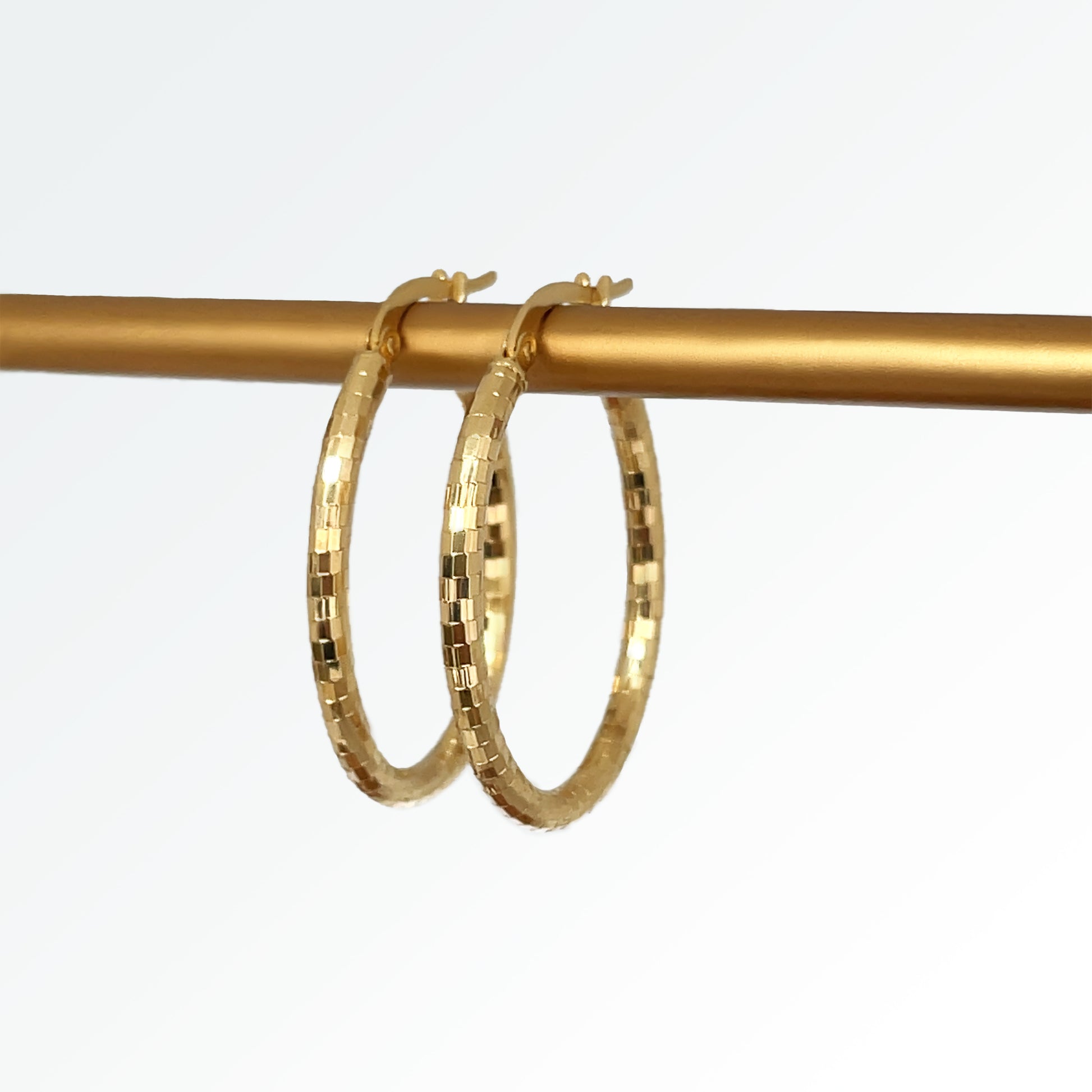 A pair of 14k gold diamond cut oval hoop earrings hanging from a gold-colored hook.